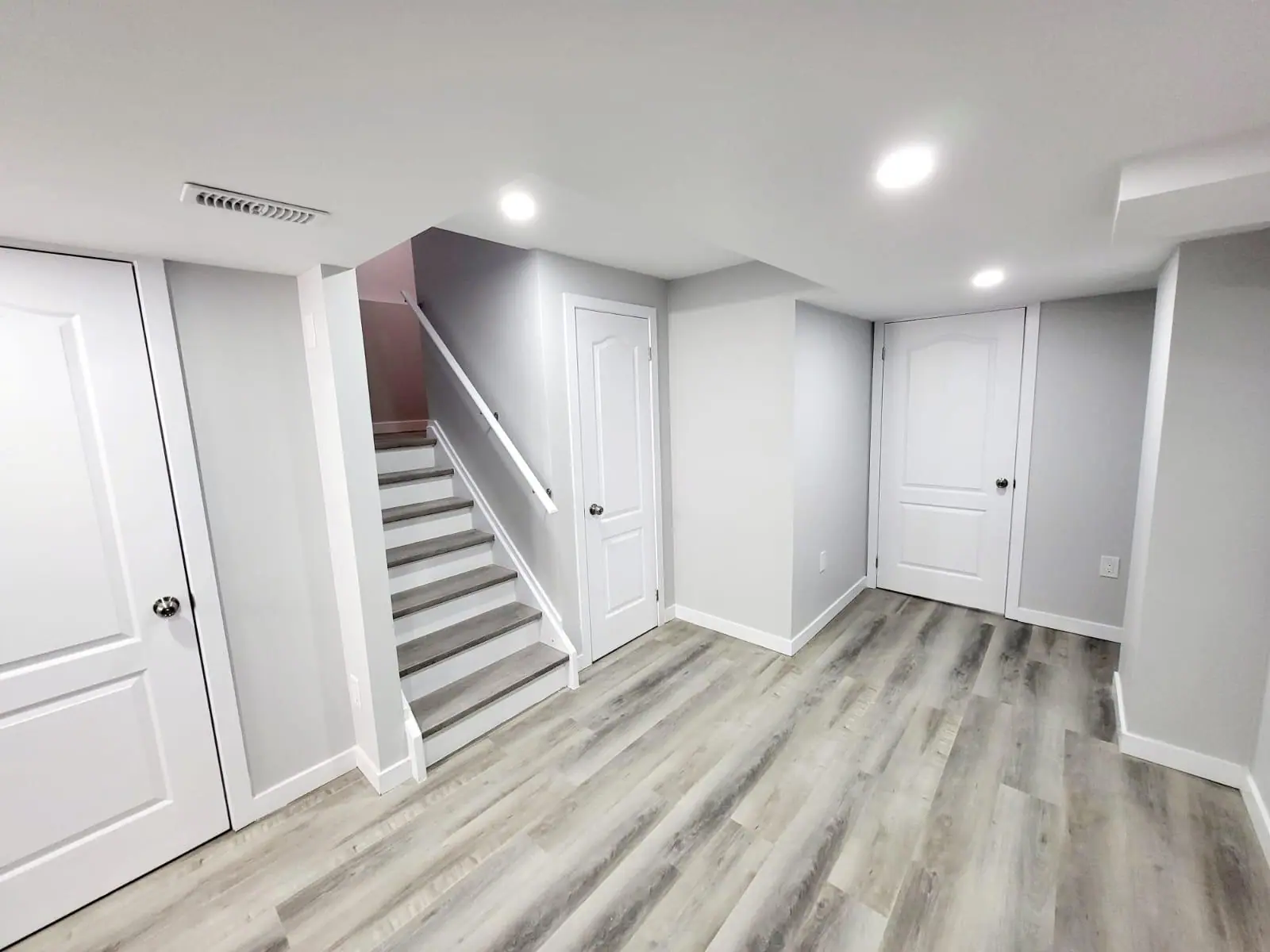 Finished basement with stairs, bedroom doors and grey vinyl plank