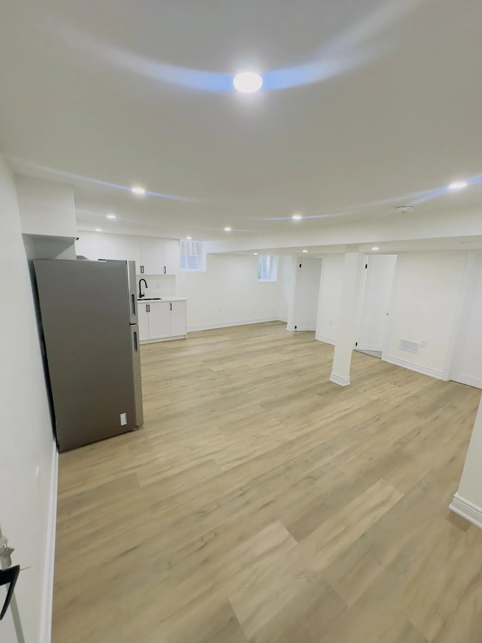 Open basement living area with stainless fridge and pot lights