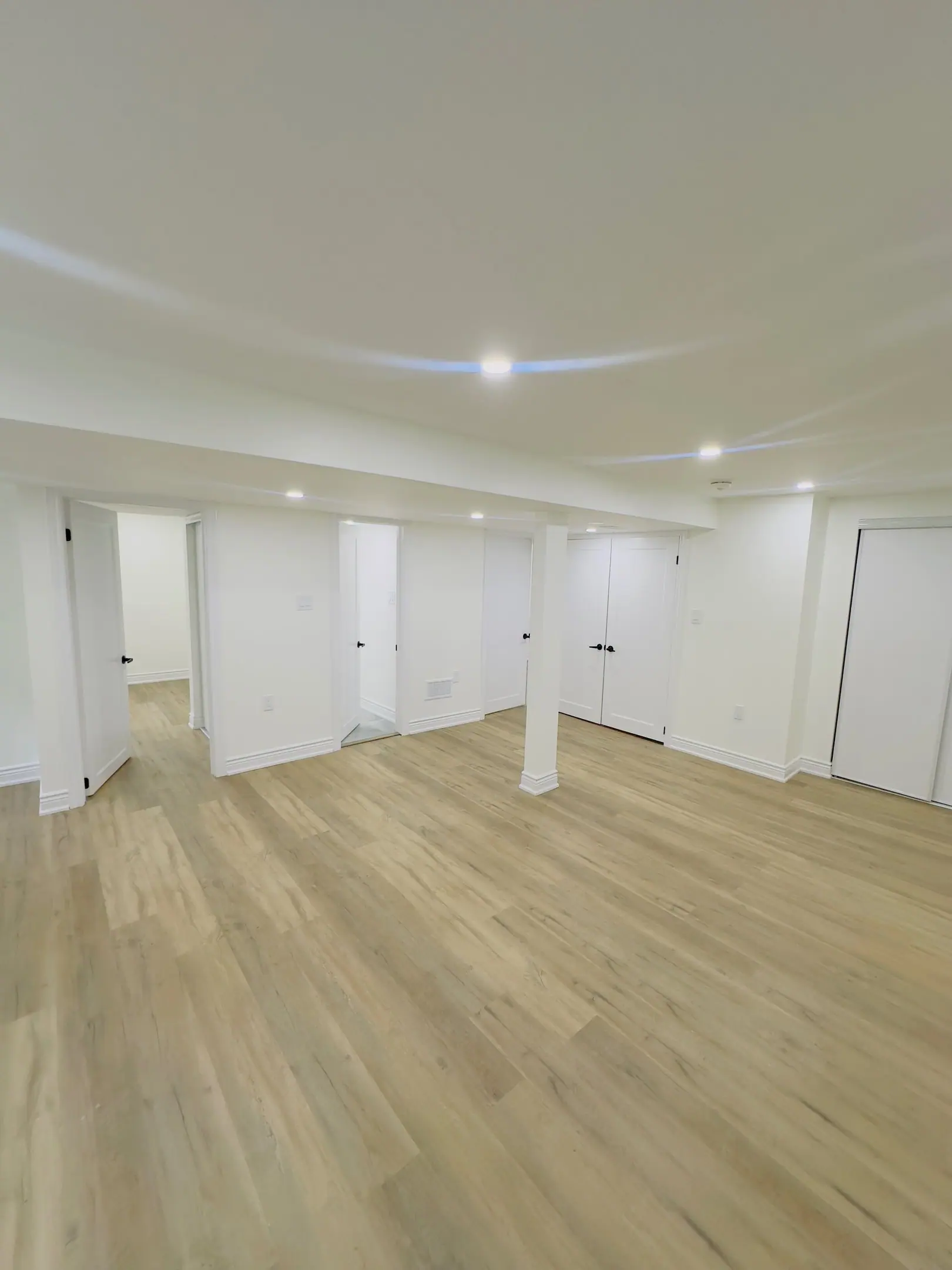 Open finished basement with light vinyl plank flooring and recessed lighting