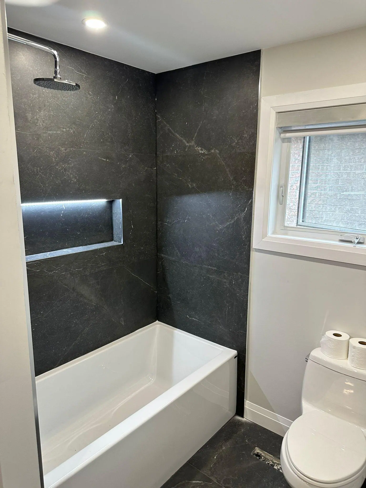 Bathtub with dark tile surround and lit niche