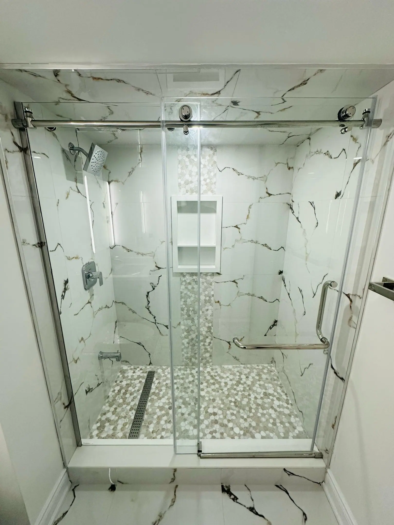 Frameless glass shower with marble tile and pebble floor
